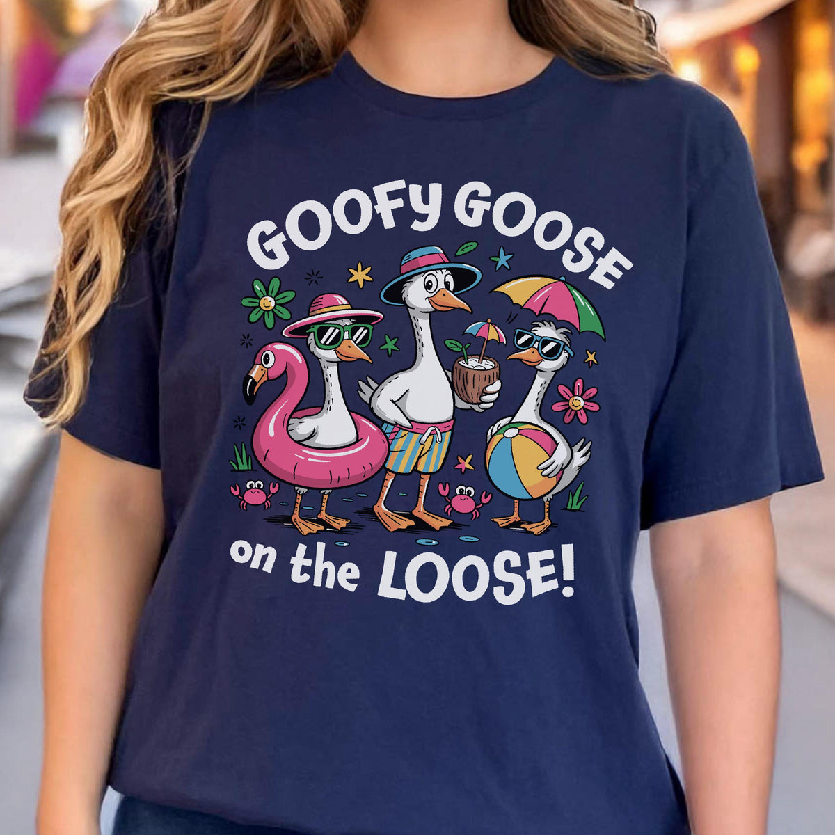 May include: Navy blue t-shirt featuring a whimsical design of three geese enjoying a beach day. The geese wear sunglasses, hats, and swimsuits, with the text "GOOFY GOOSE on the LOOSE!" above and below the illustration.