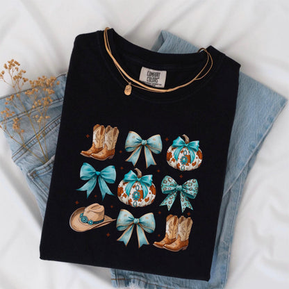 May include: Black Comfort Colors t-shirt featuring a design with cowboy boots, turquoise bows, pumpkins, and a cowboy hat. A gold necklace is draped across the shirt. The shirt is laid on top of a pair of blue jeans.
