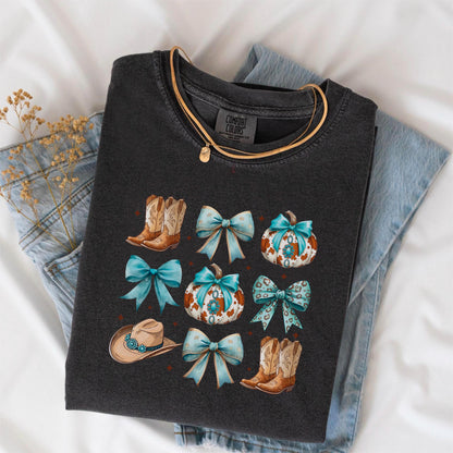 May include: Dark gray Comfort Colors t-shirt featuring a design with cowboy boots, turquoise bows, pumpkins, and a cowboy hat. A gold necklace is draped over the shirt, which is laid on top of blue jeans.