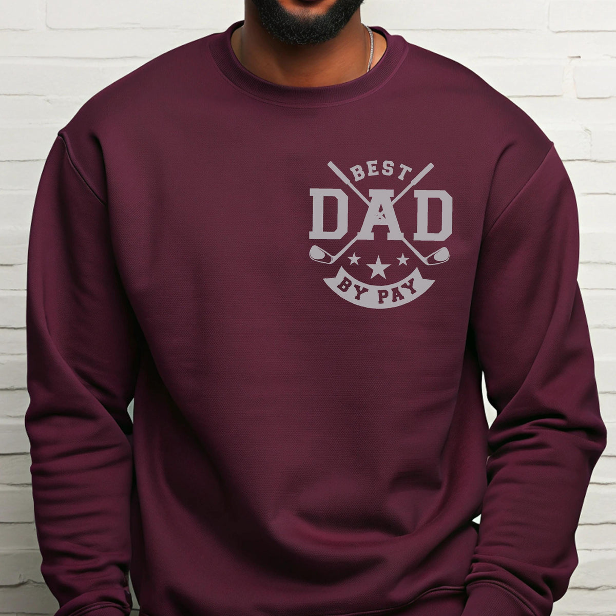 May include: A maroon sweatshirt with a gray graphic that reads "BEST DAD BY PAY". The graphic includes crossed golf clubs, stars, and the word "DAD" in bold letters. The sweatshirt is a solid color and has a crew neck.