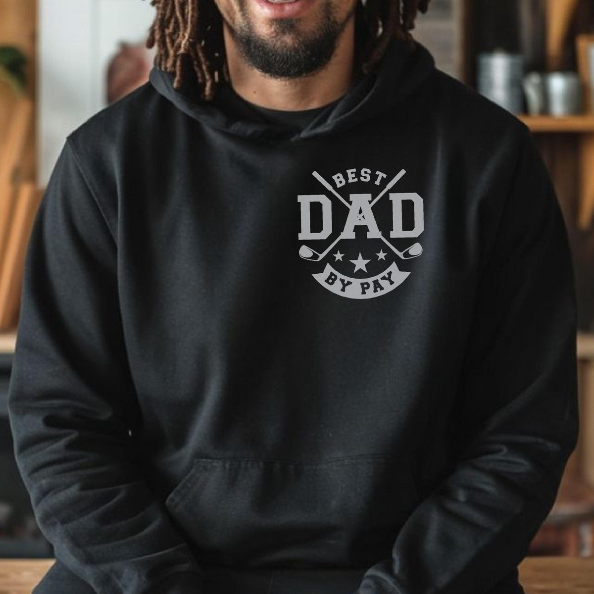 May include: Black hoodie with a gray graphic that reads "BEST DAD BY PAY" in a circular design with golf clubs and stars. The hoodie has a front pocket and a hood. The person wearing the hoodie is smiling.