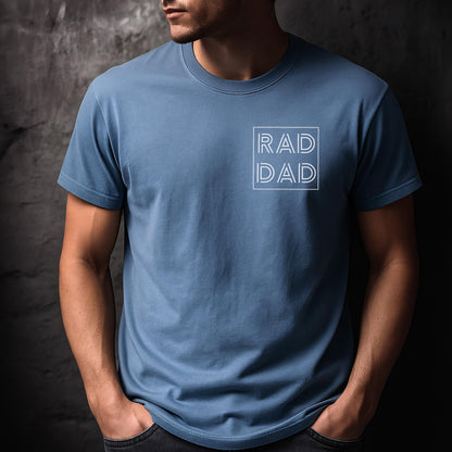 May include: A light blue t-shirt with the text "RAD DAD" in a white square. The shirt has short sleeves and a crew neck. The person is wearing dark jeans.