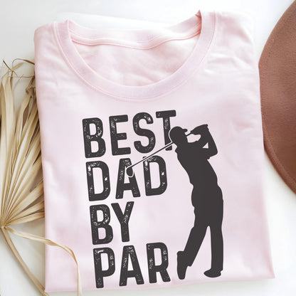 May include: A light pink t-shirt featuring a black graphic print of a golfer in a swing pose. The text "BEST DAD BY PAR" is printed in a bold, distressed black font to the left of the golfer silhouette. The shirt has a crew neckline.