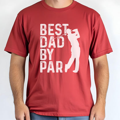 May include: A red short-sleeved t-shirt featuring a white graphic print. The design includes the text "BEST DAD BY PAR" in a distressed font, accompanied by a silhouette of a golfer swinging a club, positioned to the right of the text.