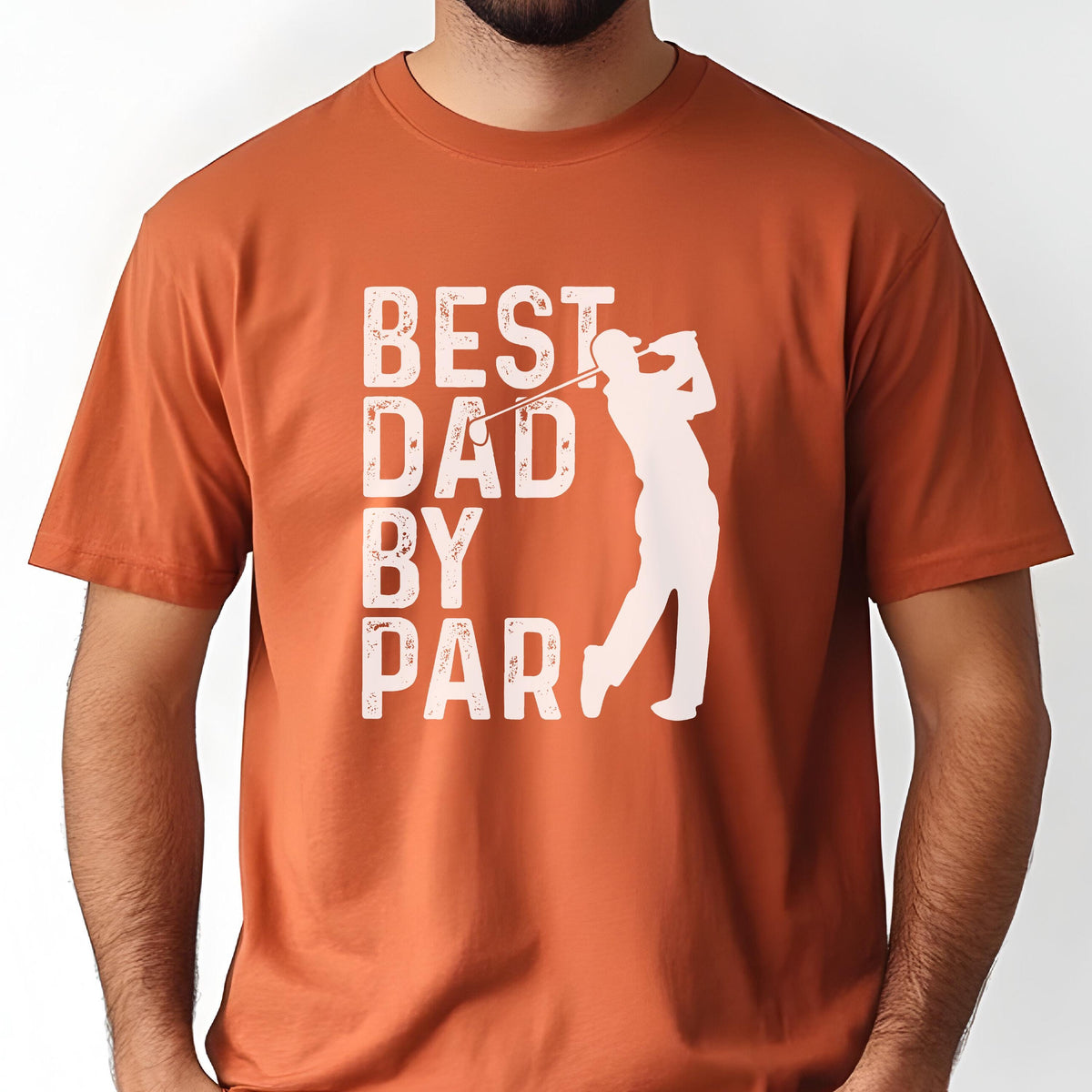 May include: A burnt orange short-sleeved t-shirt featuring a white graphic print. The design includes the text "BEST DAD BY PAR" in a distressed, block-style font next to a white silhouette of a golfer in a mid-swing position with a golf club.