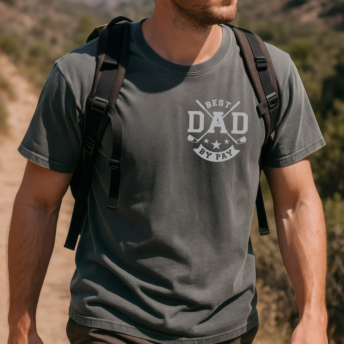 May include: A dark gray t-shirt with the text "BEST DAD BY PAR" in white. The design includes crossed golf clubs, stars, and golf balls. The shirt is short-sleeved and appears to be made of a soft material.