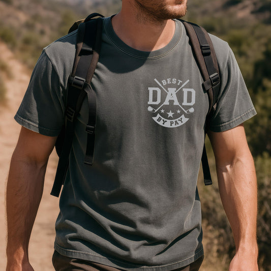 May include: A dark gray t-shirt with the text "BEST DAD BY PAR" in white. The design includes crossed golf clubs, stars, and golf balls. The shirt is short-sleeved and appears to be made of a soft material.