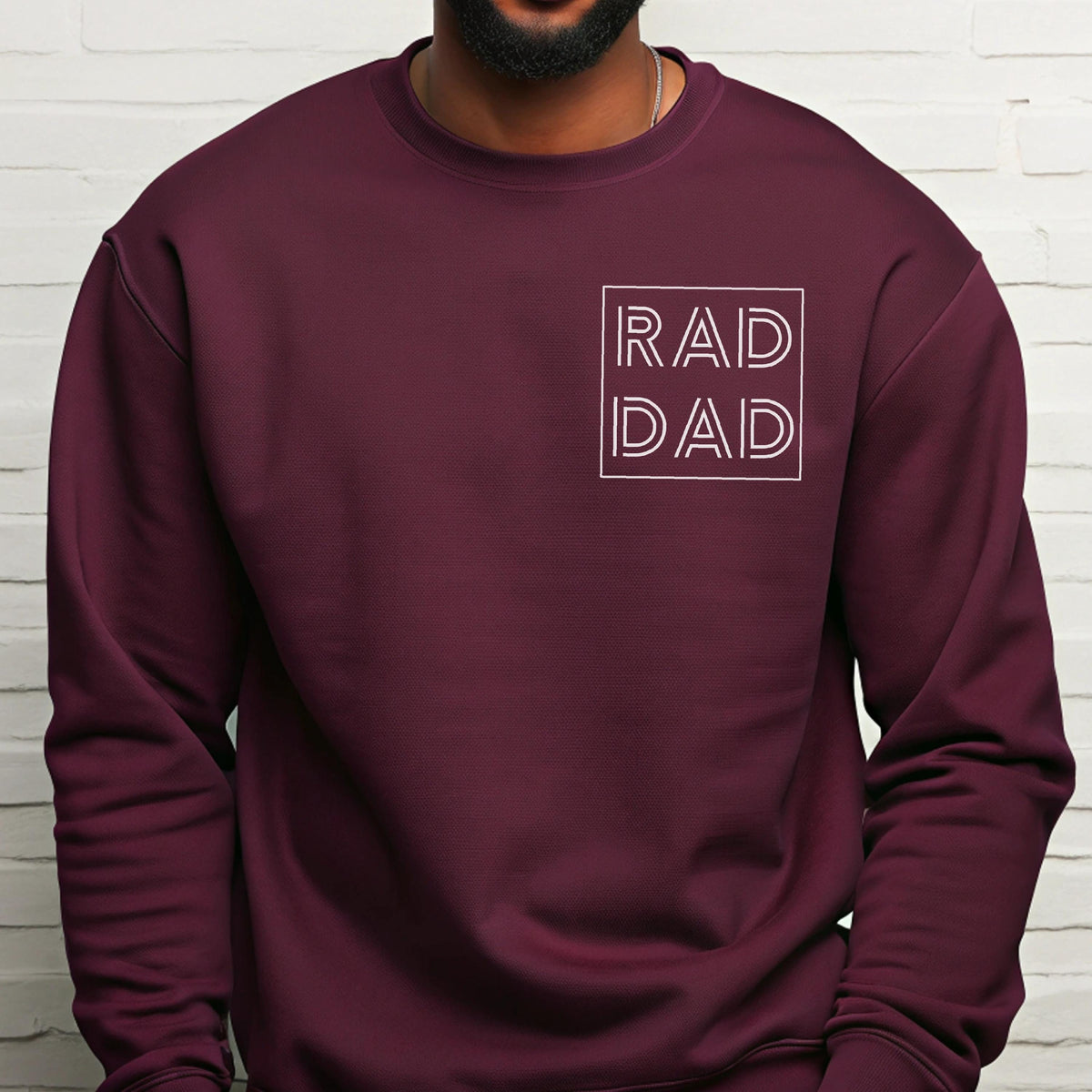 May include: A maroon crewneck sweatshirt with the words "RAD DAD" in a white, outlined font. The text is centered on the chest within a white square. The sweatshirt is a solid color and appears to be made of a soft material.