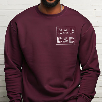 May include: A maroon crewneck sweatshirt with the words "RAD DAD" in a white, outlined font. The text is centered on the chest within a white square. The sweatshirt is a solid color and appears to be made of a soft material.