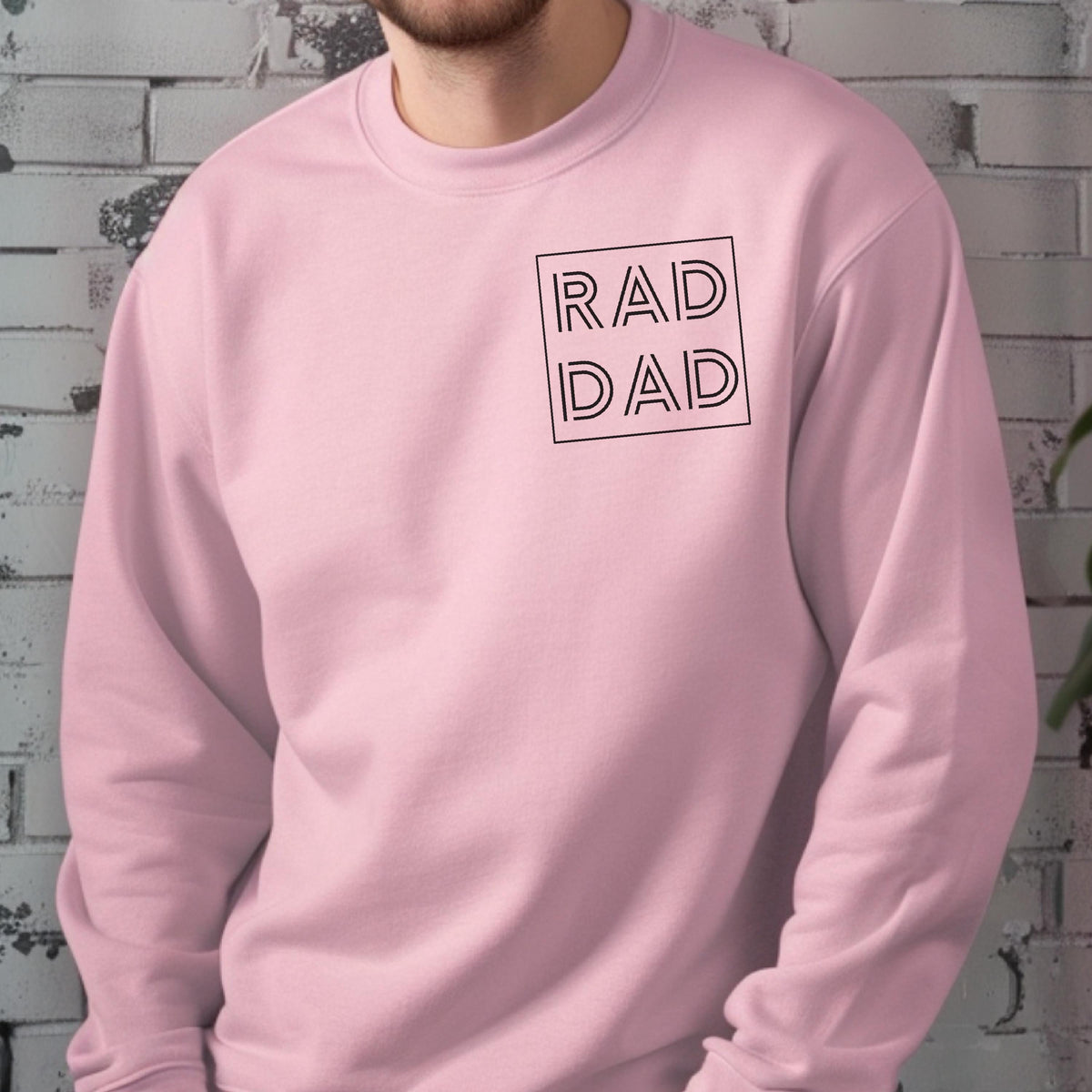 May include: A light pink sweatshirt with the words "RAD DAD" in a black, square design on the upper left chest. The sweatshirt is a solid color and has a crew neck.