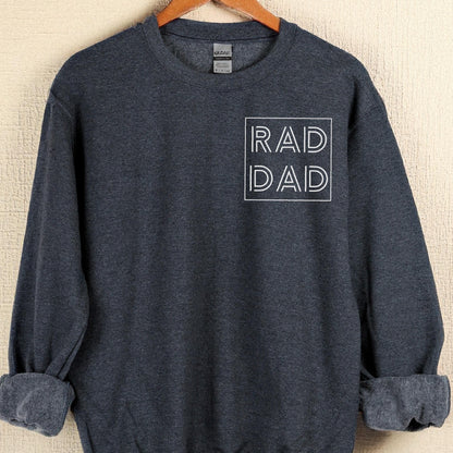 May include: A dark gray sweatshirt with the words "RAD DAD" in a white, outlined font. The sweatshirt is hanging on a wooden hanger. The sleeves are cuffed.