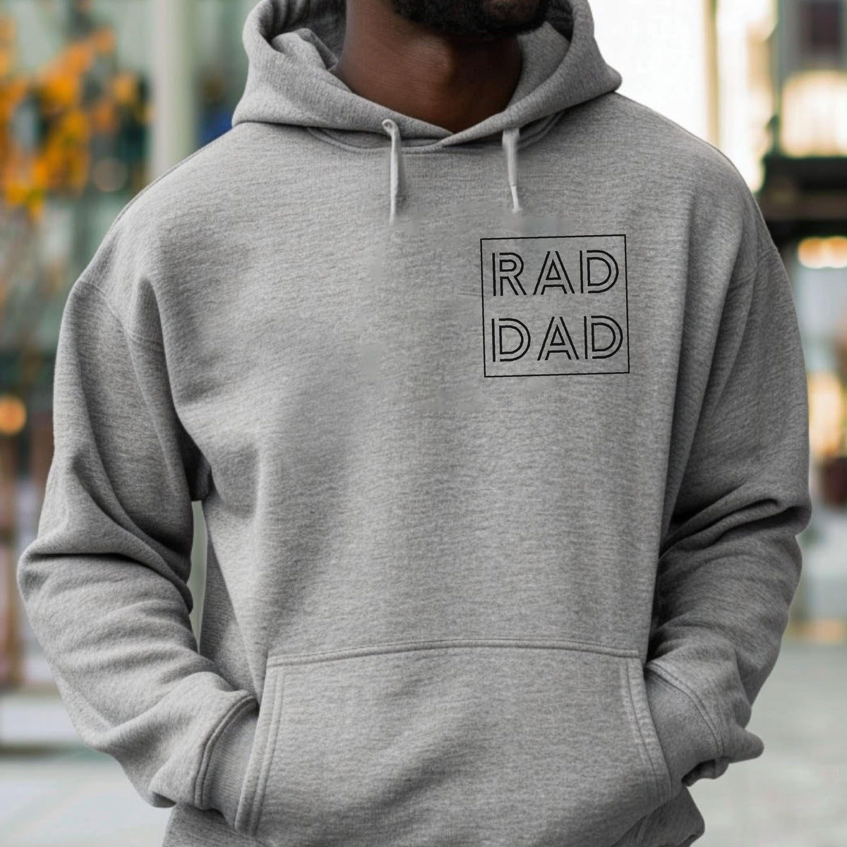 May include: A gray hoodie with a front pocket and a drawstring hood. The hoodie features the text "RAD DAD" in a black, outlined font within a square on the chest.