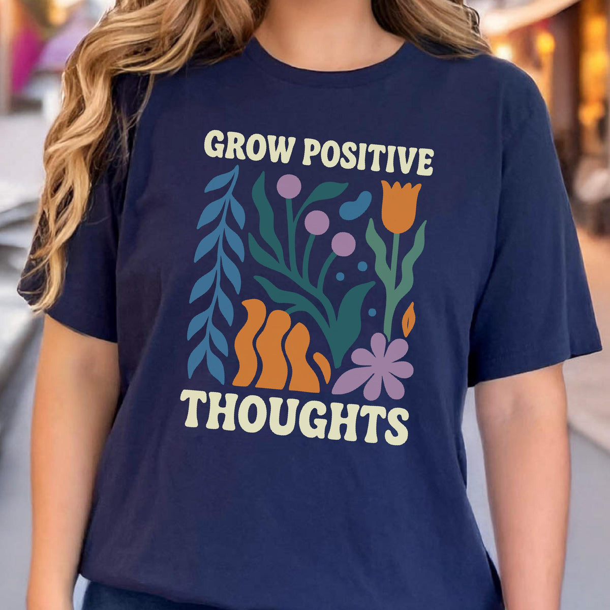 May include: Navy blue t-shirt with the text "GROW POSITIVE THOUGHTS" in a cream color. The shirt features a colorful floral design with orange, purple, and green elements.