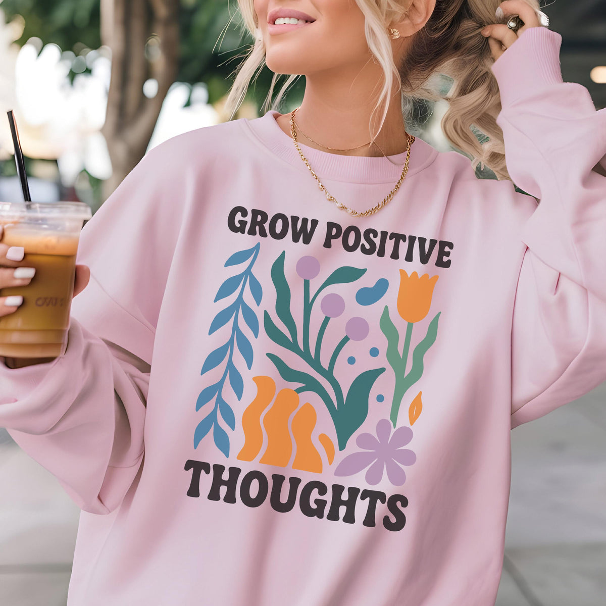 May include: A light pink sweatshirt with the words "GROW POSITIVE THOUGHTS" in a retro font. The graphic features colorful floral and leaf designs in blue, orange, green, and purple. The sweatshirt has long sleeves and a crew neck.