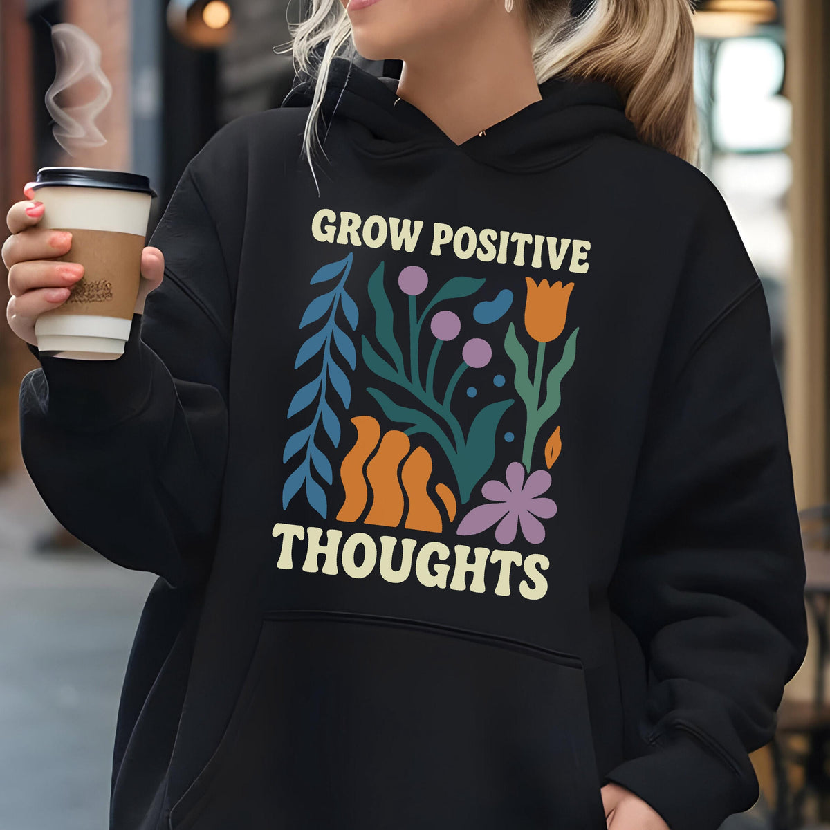 May include: Black hoodie with the words "GROW POSITIVE THOUGHTS" in white. The design includes colorful floral elements in blue, orange, purple, and green. The hoodie has a drawstring hood and a front pocket.