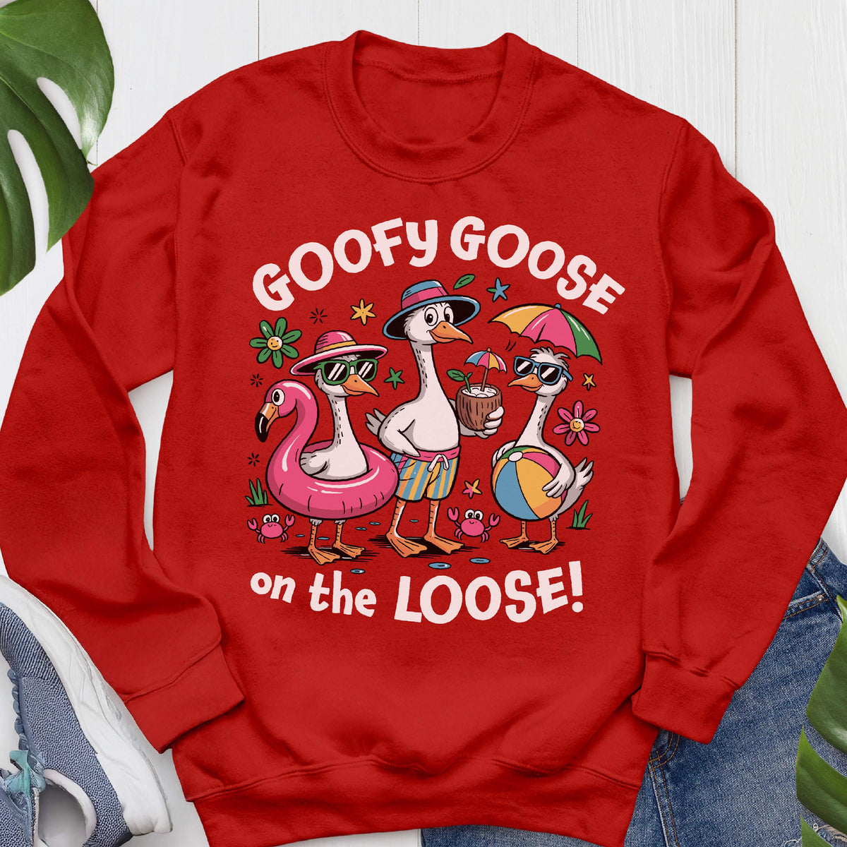 May include: Red sweatshirt with a graphic of three cartoon geese in sunglasses, beach attire, and accessories. The geese are on a flamingo float, holding a coconut drink, and a beach ball. Text reads "GOOFY GOOSE on the LOOSE!"