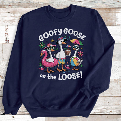 May include: Navy blue sweatshirt featuring a cartoon illustration of three geese enjoying a beach day. One goose is in a flamingo floatie, another holds a coconut drink, and the third has a beach ball. The text "GOOFY GOOSE on the LOOSE!" is above the geese.