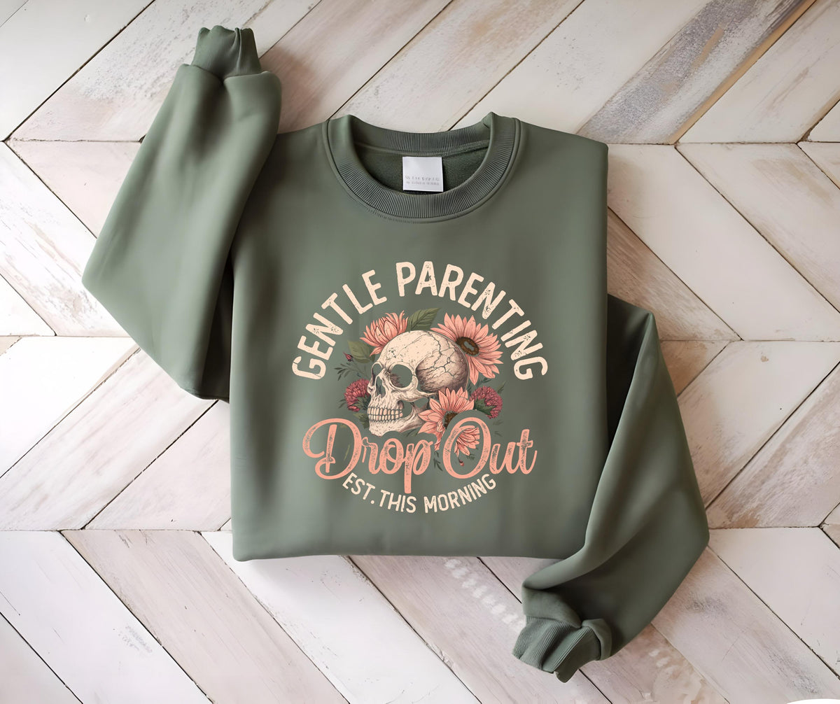 May include: Olive green sweatshirt with the text "GENTLE PARENTING Drop Out EST. THIS MORNING" and a skull graphic surrounded by flowers. The long-sleeved top is made of a soft material.