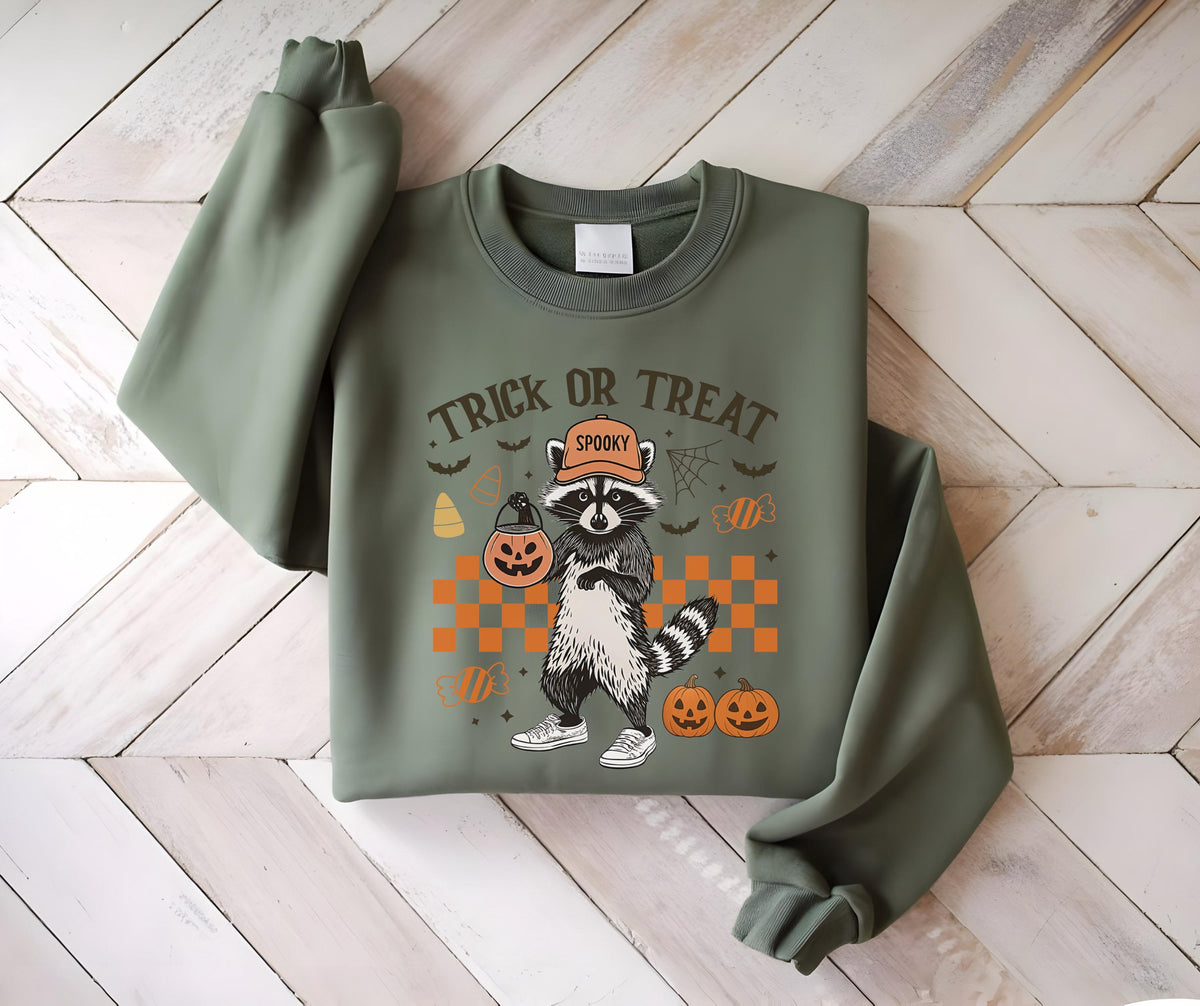 May include: Olive green sweatshirt featuring a Halloween-themed graphic. The design includes a raccoon wearing a hat and holding a jack-o'-lantern, with the words "Trick or Treat" above. Additional Halloween elements like pumpkins and bats are also present.