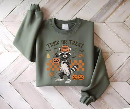 May include: Olive green sweatshirt featuring a Halloween-themed graphic. The design includes a raccoon wearing a hat and holding a jack-o'-lantern, with the words "Trick or Treat" above. Additional Halloween elements like pumpkins and bats are also present.