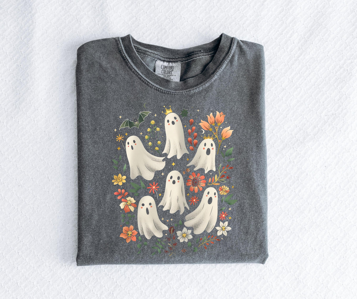 May include: A dark gray t-shirt featuring a whimsical design of several white cartoon ghosts with floral and bat accents. Some ghosts wear crowns. The design includes orange, yellow, and red flowers.