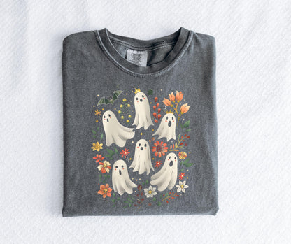 May include: A dark gray t-shirt featuring a whimsical design of several white cartoon ghosts with floral and bat accents. Some ghosts wear crowns. The design includes orange, yellow, and red flowers.