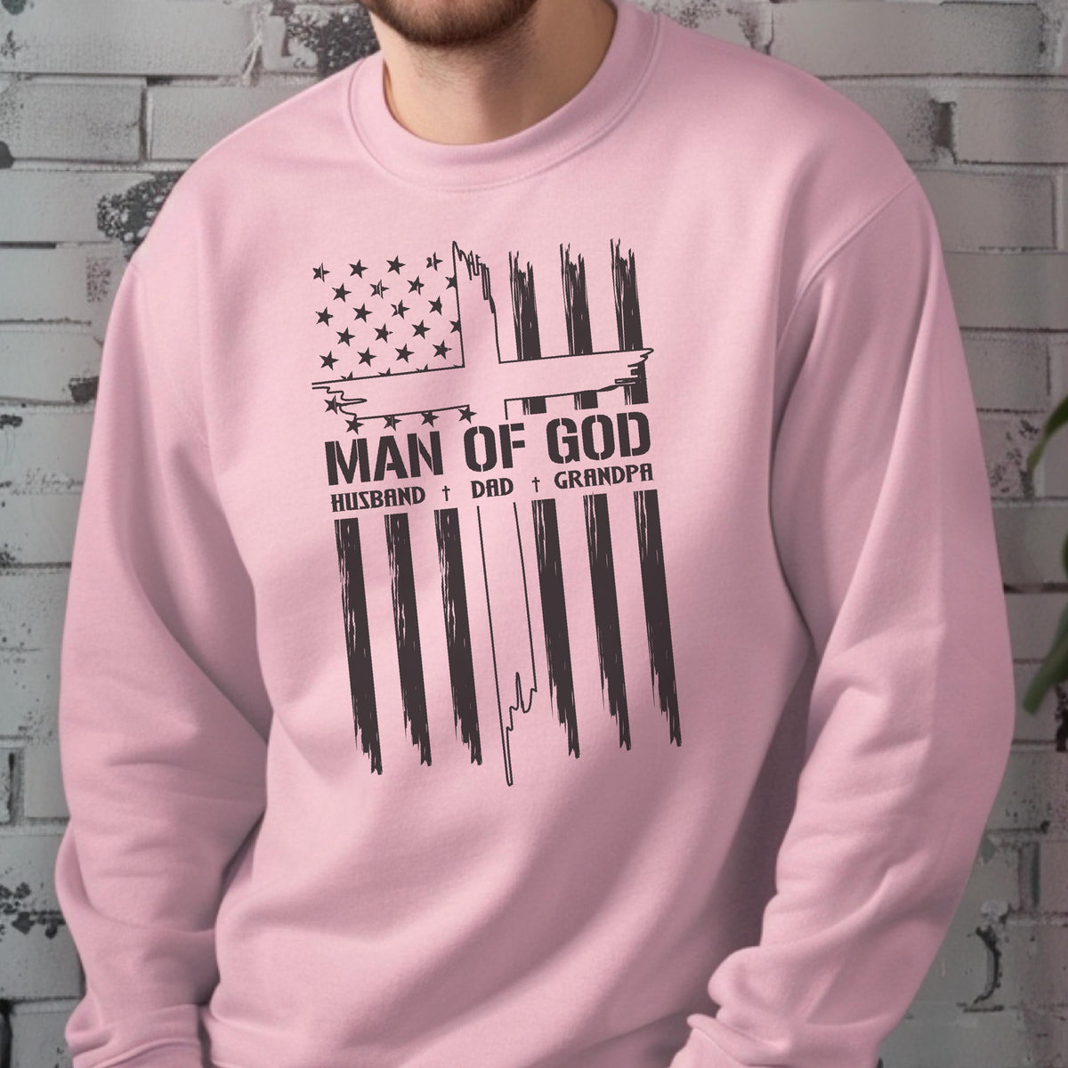 May include: A light pink sweatshirt with a graphic design. The design features a cross and the American flag with the words "MAN OF GOD" and the words "HUSBAND, DAD, GRANDPA" in black.