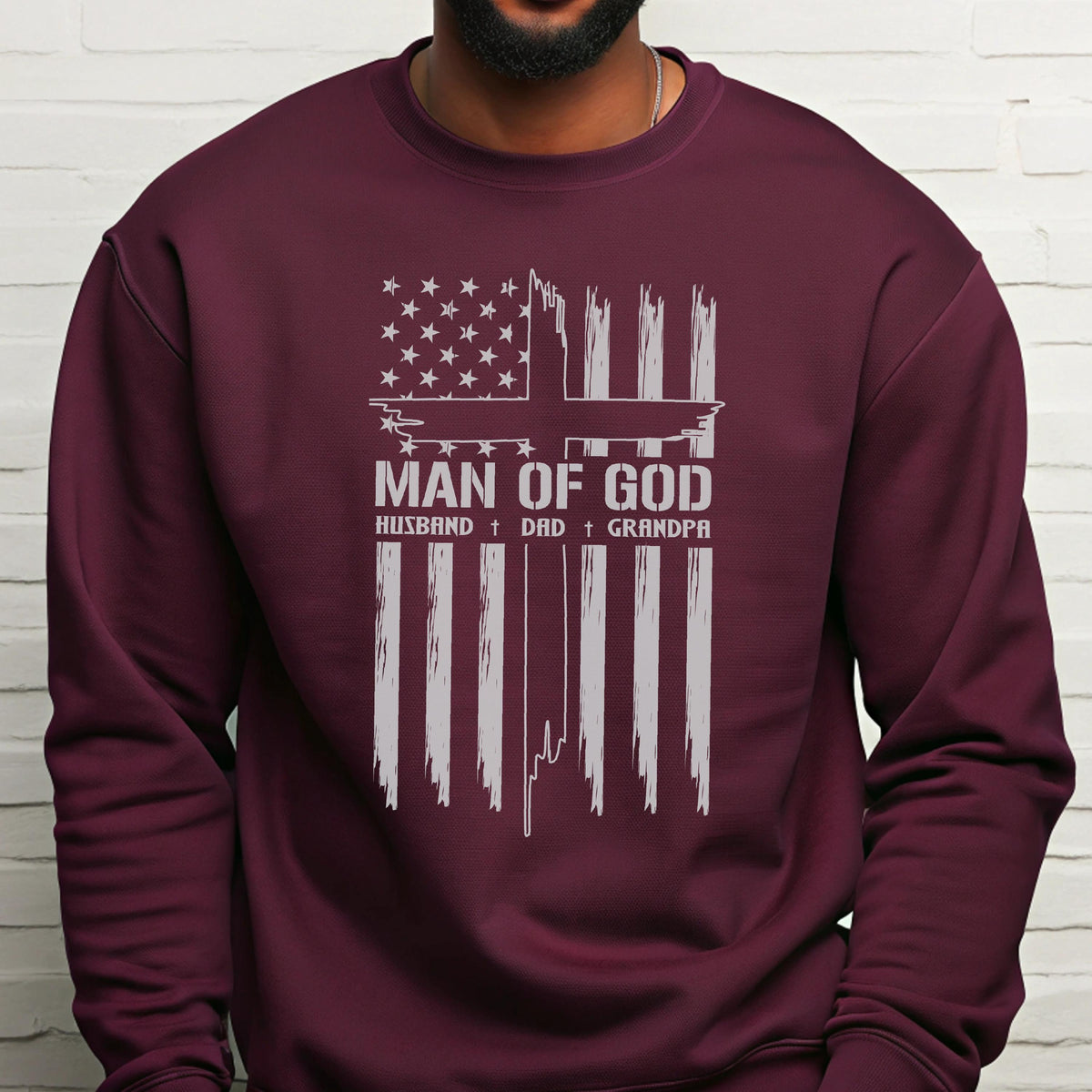 May include: Burgundy sweatshirt with a white graphic design. The design features an American flag with a cross and the words "MAN OF GOD" above "HUSBAND + DAD + GRANDPA". The sweatshirt is made of a soft material.