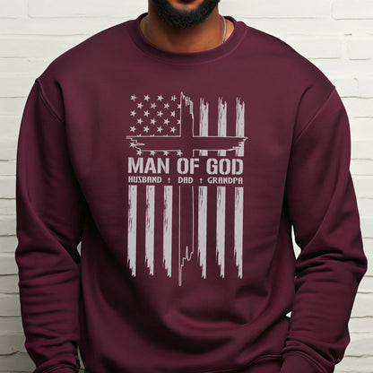 May include: Burgundy sweatshirt with a white graphic design. The design features an American flag with a cross and the words "MAN OF GOD" above "HUSBAND + DAD + GRANDPA". The sweatshirt is made of a soft material.