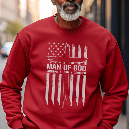 May include: A red sweatshirt with a white graphic design. The design features an American flag with a cross, the words "MAN OF GOD," and the words "HUSBAND + DAD + GRANDPA."