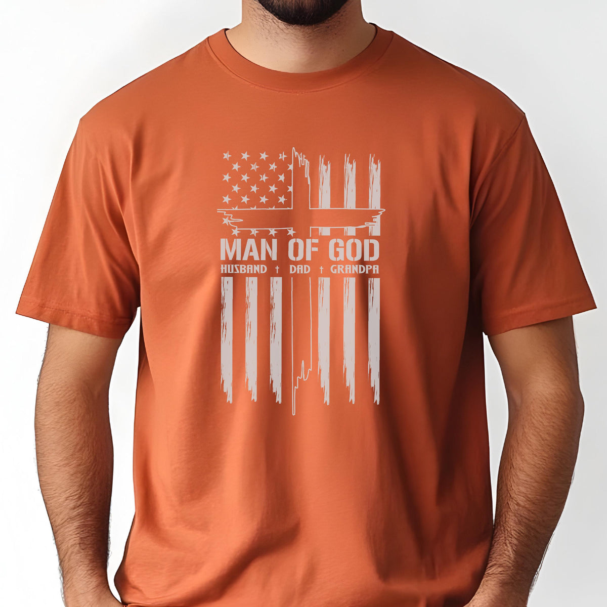 May include: Orange t-shirt featuring a distressed American flag design with a cross and the words "MAN OF GOD." Below the text are the words "HUSBAND, DAD, GRANDPA."