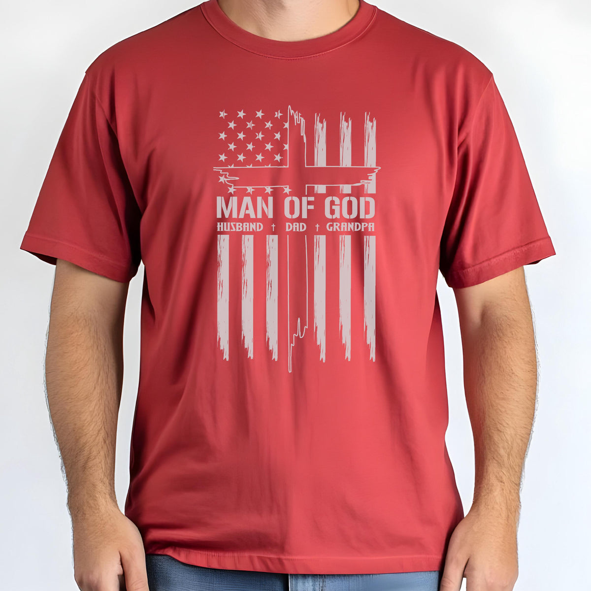 May include: Red t-shirt featuring a distressed American flag design with the text "MAN OF GOD" and the words "HUSBAND + DAD + GRANDPA" in a white, vintage font. The shirt is short-sleeved and has a crew neck.