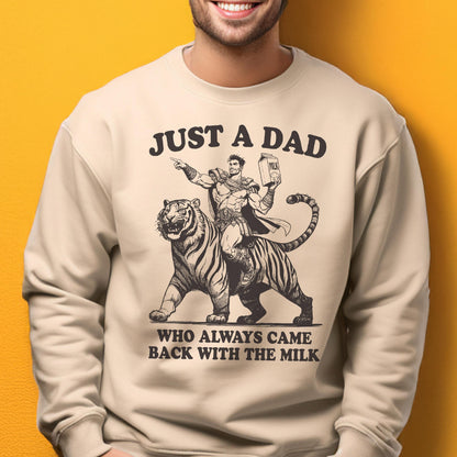 May include: Beige sweatshirt with a graphic of a superhero riding a tiger, holding a milk carton. Text reads "JUST A DAD WHO ALWAYS CAME BACK WITH THE MILK" in black. The design is a humorous take on fatherhood.