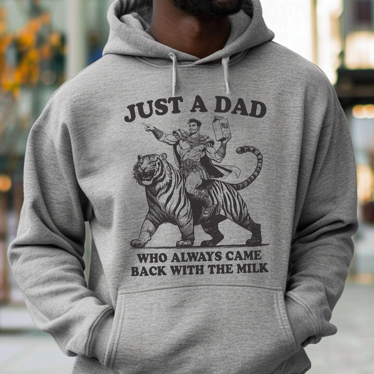May include: Gray hoodie with the text "JUST A DAD WHO ALWAYS CAME BACK WITH THE MILK." The graphic depicts a man riding a tiger, holding a milk carton. The hoodie has a drawstring hood and a front pocket.