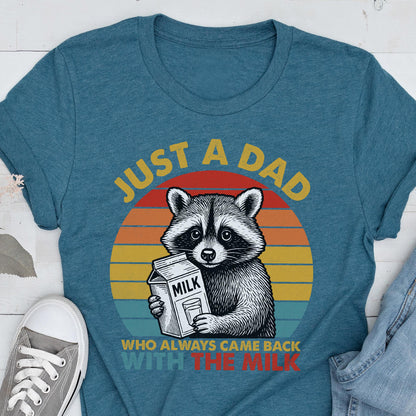 May include: Teal t-shirt with a graphic of a raccoon holding a milk carton. The text reads "JUST A DAD WHO ALWAYS CAME BACK WITH THE MILK" in yellow and red. The raccoon is set against a sunset background.