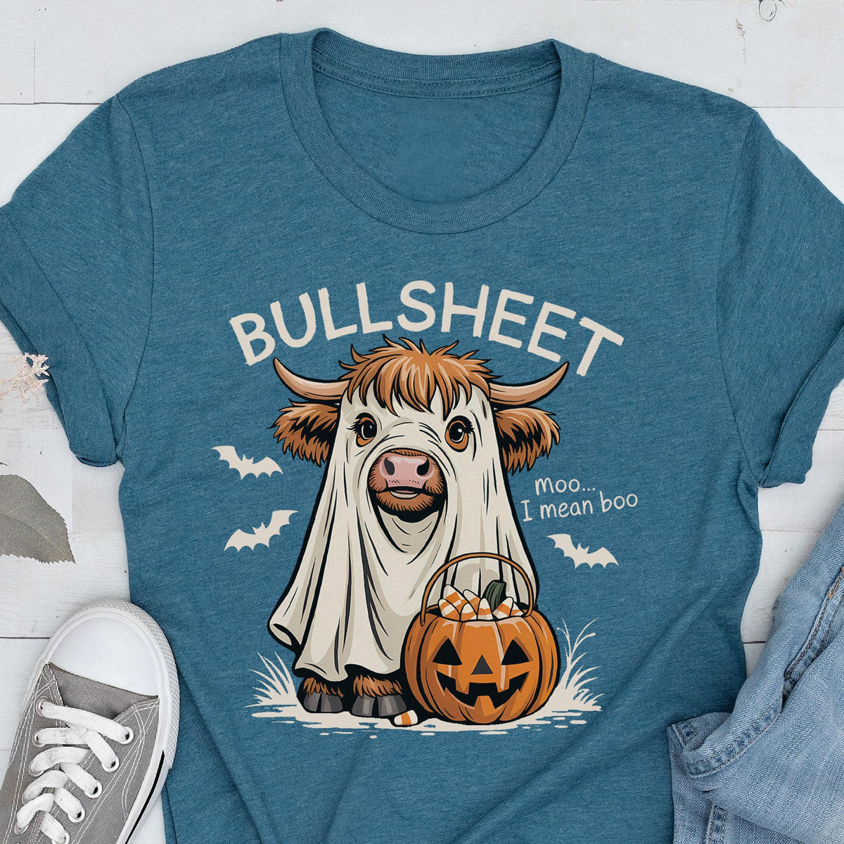 May include: Teal t-shirt featuring a cartoon cow dressed as a ghost, holding a jack-o'-lantern filled with candy corn. The text "BULLSHEET" is above the cow, with "moo... I mean boo" below. Bats are also featured.