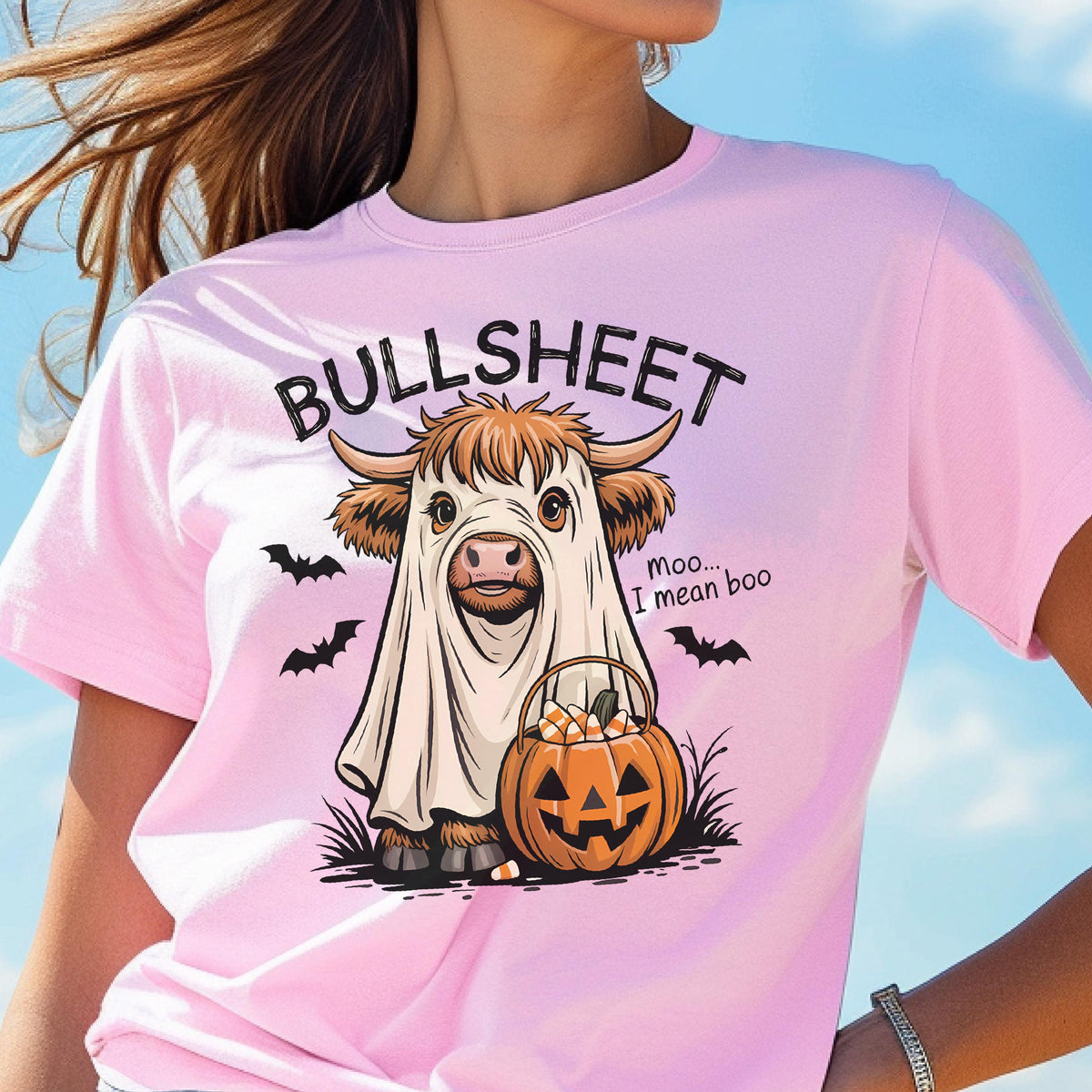 May include: Pink t-shirt with a Halloween-themed graphic. The design features a cow dressed as a ghost with the text "BULL SHEET" above and "moo... I mean boo" below. A jack-o'-lantern and bats complete the design.