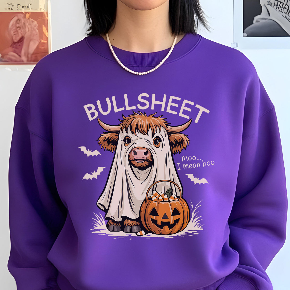 May include: A purple sweatshirt featuring a cartoon cow dressed as a ghost with the word "BULLSHEET" above it. The cow is holding a jack-o'-lantern filled with candy corn. The phrase "Moo... I mean boo" is also printed on the shirt.