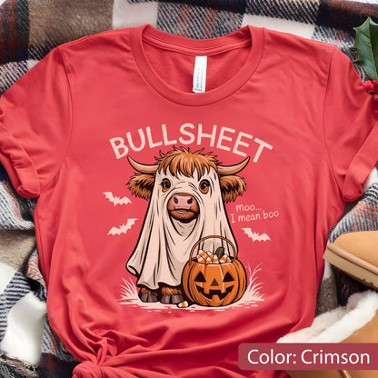 May include: A crimson t-shirt featuring a graphic of a Highland cow wearing a white ghost sheet. The text reads BULLSHEET and moo... I mean boo. The cow holds a jack-o'-lantern pumpkin bucket filled with candy corn, surrounded by small white bats.