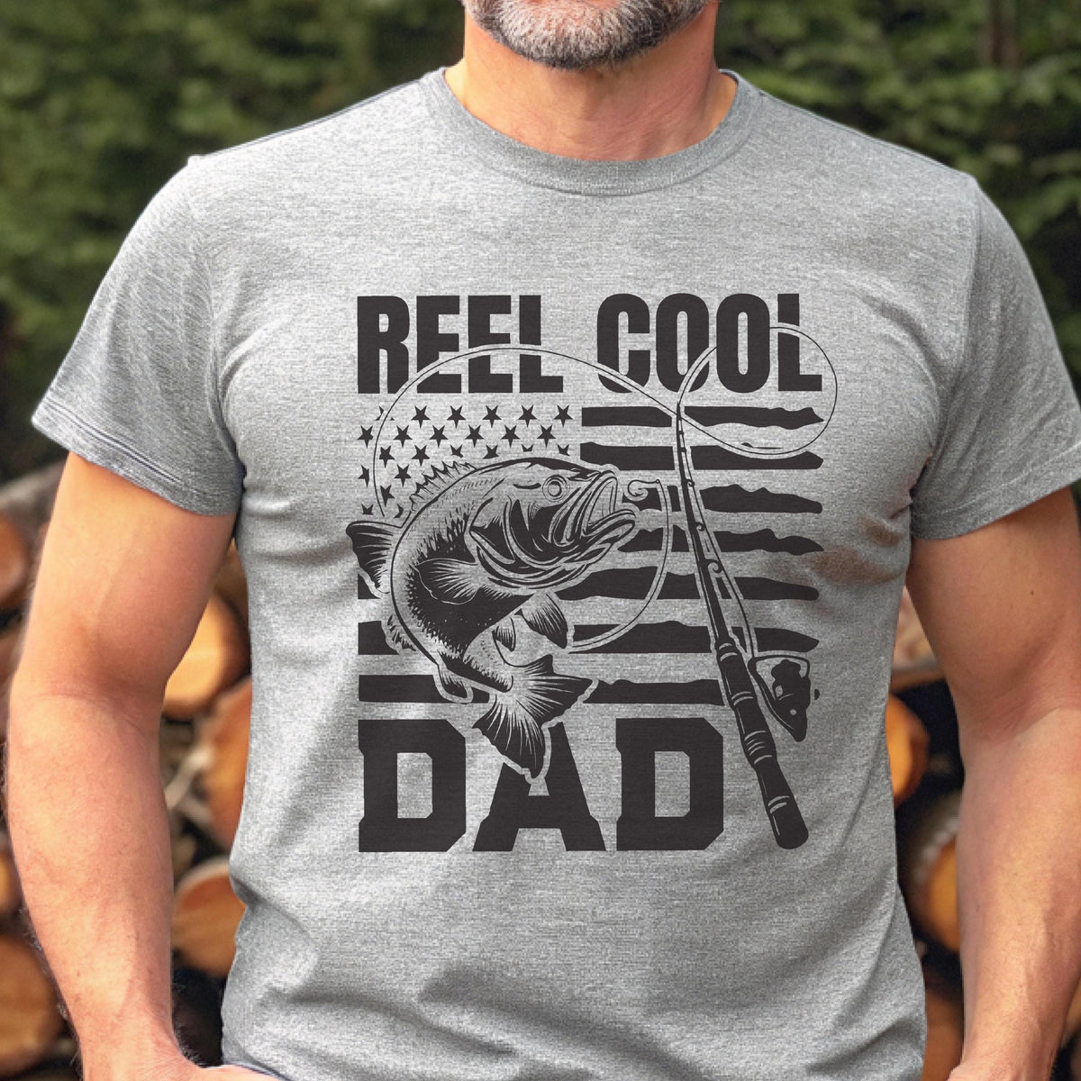 May include: A gray t-shirt with the words "REEL COOL DAD" in black block letters. The design includes a fish, fishing rod, and an American flag motif. The shirt is short-sleeved and made of a soft material.