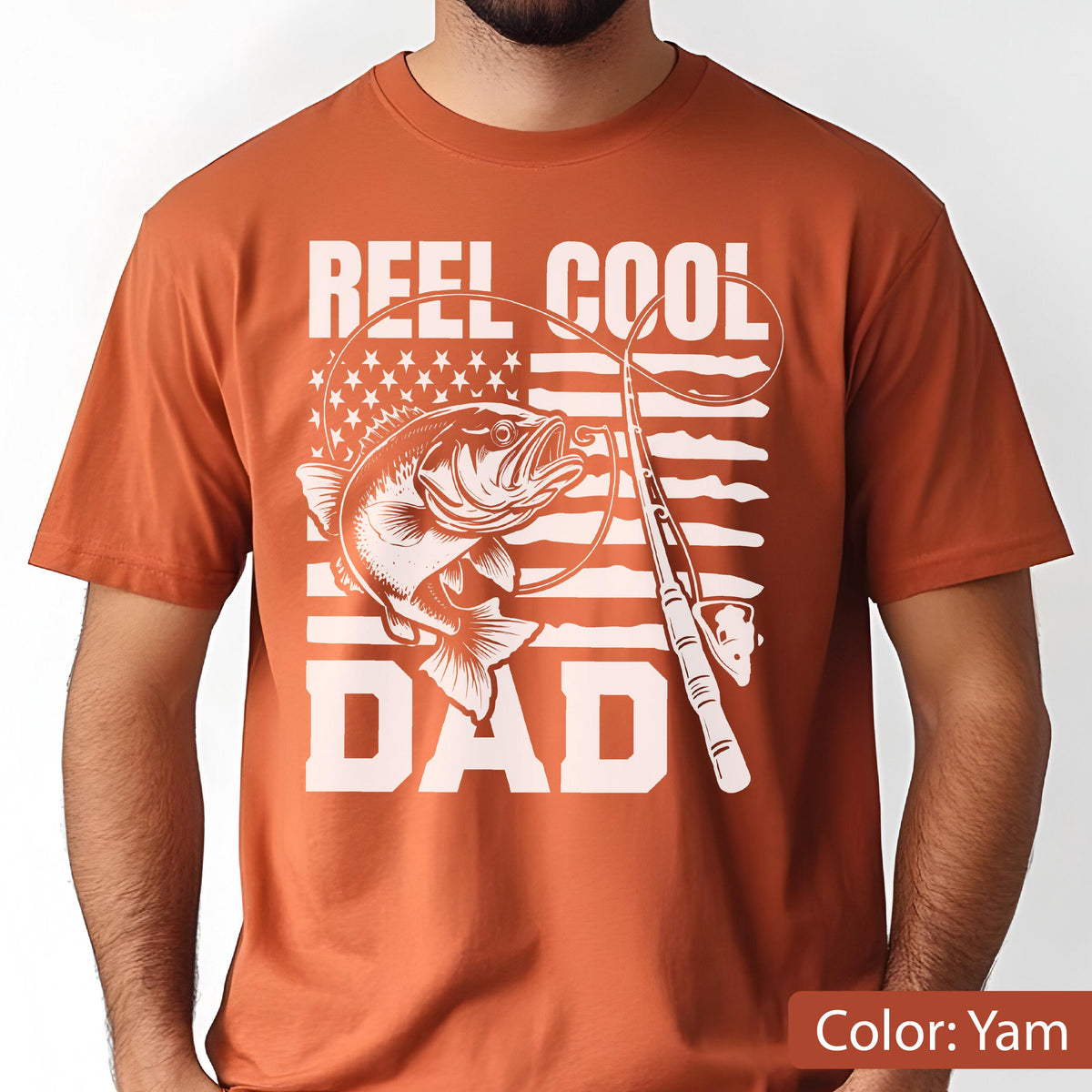 May include: Yam-colored t-shirt with a white graphic featuring a fish, fishing rod, and the text "REEL COOL DAD." The design incorporates an American flag motif. A casual tee for fishing enthusiasts.