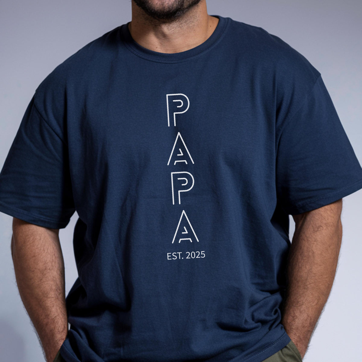 May include: Navy blue t-shirt with the word "PAPA" in white, vertically aligned text. Below the word "PAPA" is the text "EST. 2025". The shirt is a crew neck style.