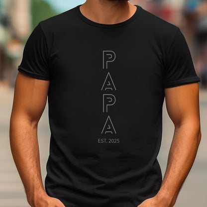 May include: Black t-shirt with the word "PAPA" in a vertical, outlined font. Below the word "PAPA" is the text "EST. 2025" in a smaller font. The shirt is a crew neck style.