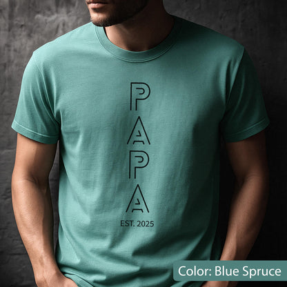 May include: Blue spruce t-shirt with the word "PAPA" in black, vertically aligned, and the text "EST. 2025" below. The shirt is a solid color and has a crew neck.