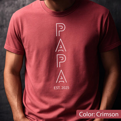 May include: Crimson-colored t-shirt with the word "PAPA" in white, vertically aligned. Below the word "PAPA" is the text "EST. 2025". The shirt is made of a soft material and has short sleeves.