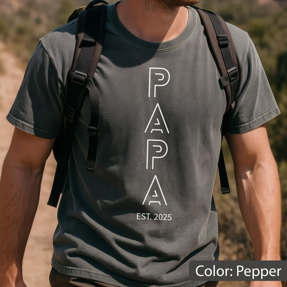 May include: Pepper-colored t-shirt with the word "PAPA" in white, vertically aligned. Below the word "PAPA" is the text "EST. 2025". The shirt has short sleeves and a crew neck. The color is described as "Pepper".