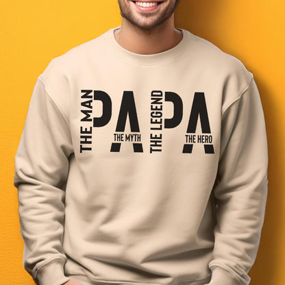 May include: Beige sweatshirt with the word "PAPA" in large black letters. The words "THE MAN", "THE MYTH", "THE LEGEND", and "THE HERO" are printed vertically on the sides of the word "PAPA".