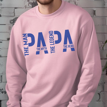 May include: A light pink sweatshirt with the word "PAPA" in blue, vertically stacked with the phrases "THE MAN", "THE MYTH", "THE LEGEND", and "THE HERO". The sweatshirt is a solid color.