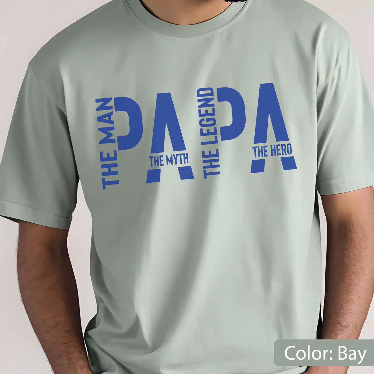 May include: A light green t-shirt with the word "PAPA" in blue, with the phrases "THE MAN", "THE MYTH", "THE LEGEND", and "THE HERO" in blue. The shirt is a solid color and has short sleeves.