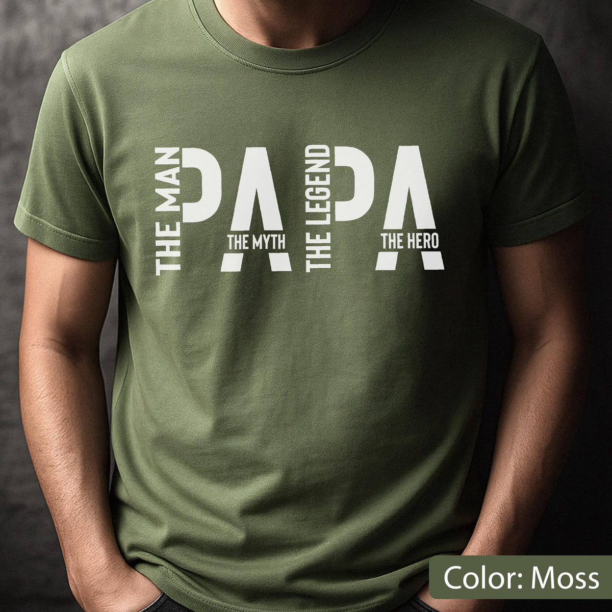 May include: A moss green t-shirt with the word "PAPA" in large white capital letters. The words "THE MAN", "THE MYTH", "THE LEGEND", and "THE HERO" are also printed on the shirt in white. The text "Color: Moss" is at the bottom.
